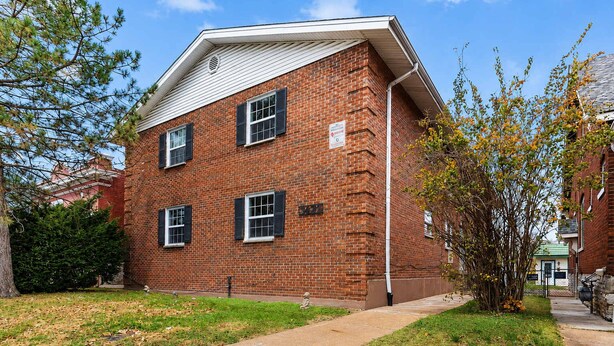 A red brick building with three windows, a small tree in front, and a clear blue sky.