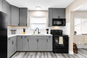 Una cocina moderna con armarios grises, un refrigerador negro, un microondas y una estufa.