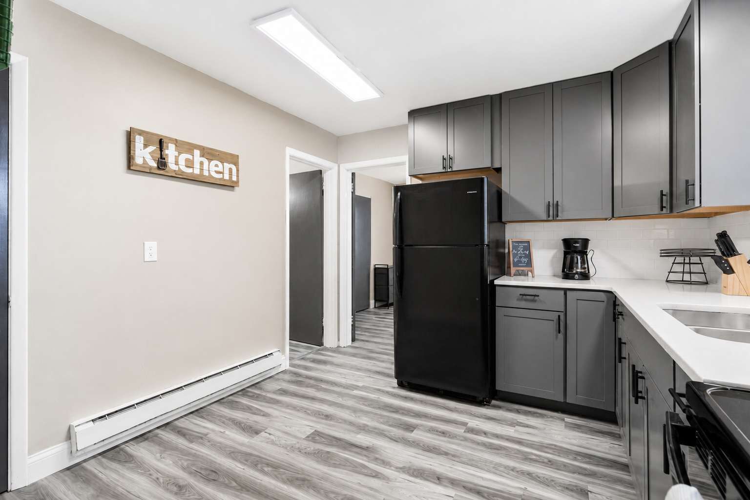 A modern kitchen with grey cabinets, a black refrigerator, and a white countertop.