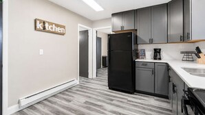 A modern kitchen with grey cabinets, a black refrigerator, and a white countertop.