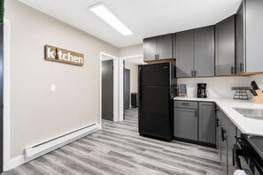A modern kitchen with grey cabinets, a black refrigerator, and a white countertop.