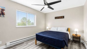 A bedroom with a bed, a ceiling fan, a window, and a sign that says 'GATHER'.