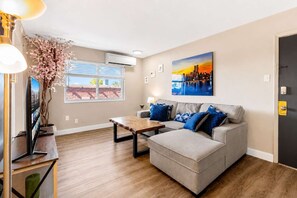 Een woonkamer met een bank, een salontafel, een televisie en een schilderij aan de muur.