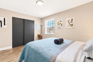 Een slaapkamer met een bed, een kledingkast, een raam met zonwering en wanddecoratie.