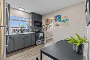 A modern kitchen with grey cabinets, a black countertop, and a black dining table with a potted plant.