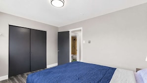 Ein Schlafzimmer mit Bett, Kleiderschrank und einem durch eine offene Tür einsehbaren Badezimmer.