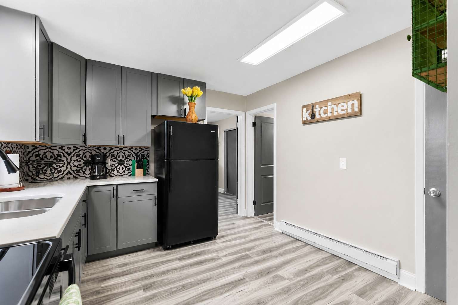 A modern kitchen with grey cabinets, a black refrigerator, and a 'kitchen' sign on the wall.