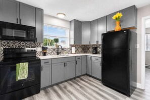 A modern kitchen with grey cabinets, a black refrigerator, a microwave, and a coffee maker. - Travel Nurse 1BR · 3 mi SSM SLU · Pet-Friendly · Long Stays (St. Louis)