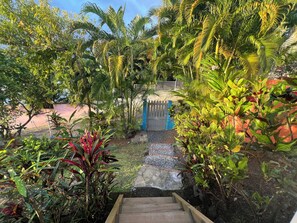 Ein Gartenweg führt zu einem verschlossenen Eingang, umgeben von üppiger Vegetation und verschiedenen Pflanzen.