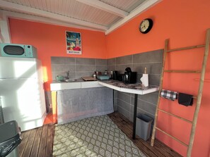 Eine kompakte Küche mit Kühlschrank, Spüle, Kaffeemaschine und einer Wanduhr.