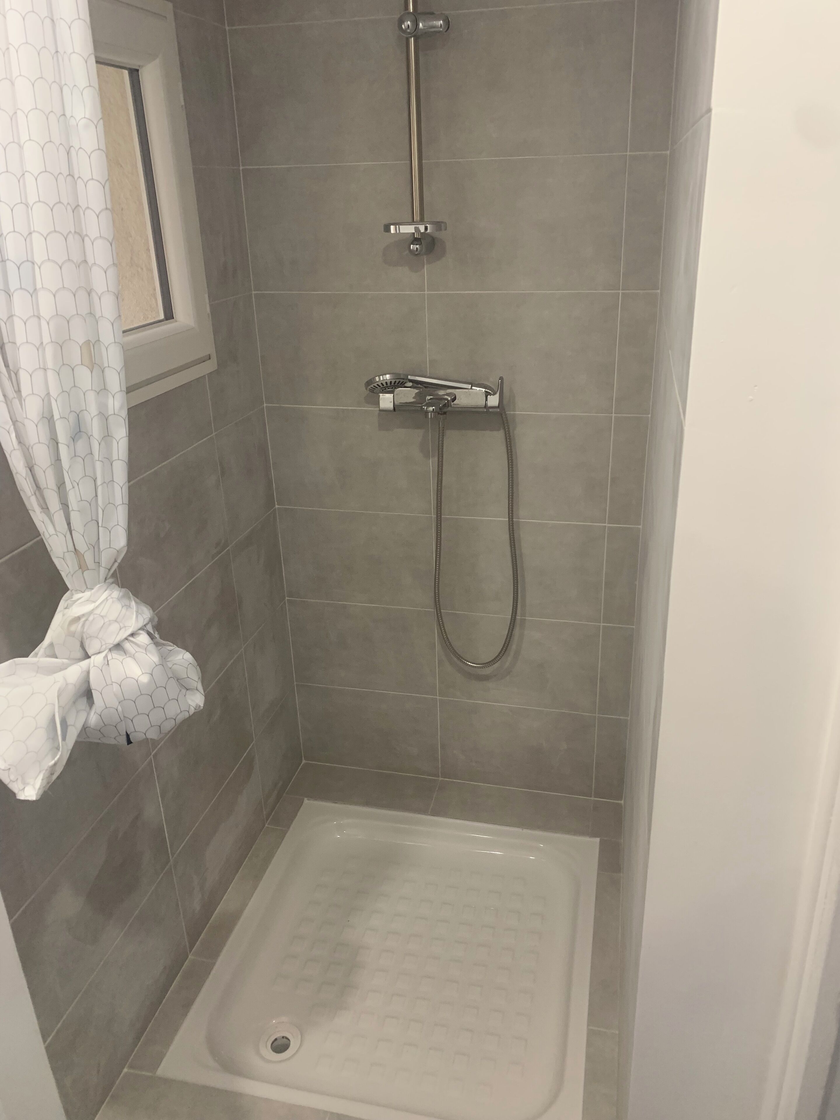 A shower stall with a handheld showerhead, a wall-mounted faucet, and a tiled floor.