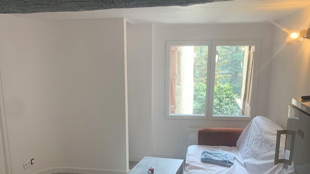 Ein Zimmer mit Bett, einem kleinen Tisch und einem Fenster mit Blick auf Grün.