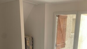 Ein Schlafzimmer mit Bett, einem Fenster mit Vorhängen, einer Heizung und einem kleinen Tisch.