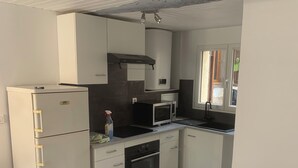 Eine kleine Küche mit Kühlschrank, Mikrowelle, Backofen und einem Fenster.