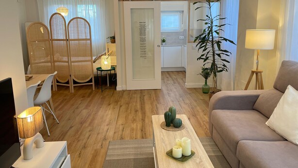 Ein modernes Wohnzimmer mit einer Couch, einem Esstisch, einem Fernseher und einer Küche im Hintergrund.