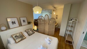 Ein Hotelzimmer mit einem Bett, einem Nachttisch mit Lampe, einem Sessel, einem Schreibtisch, einem Kleiderschrank und einer Pendelleuchte.