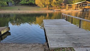 A wooden dock extending into a calm body of water, surrounded by trees and a small building. - Hidden Cove RV Site On Lake LBJ. (Kingsland)