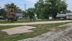 A residential area with a driveway, a palm tree, a large tree, and a house with a garage. - Hidden Cove RV Site On Lake LBJ. (Kingsland)
