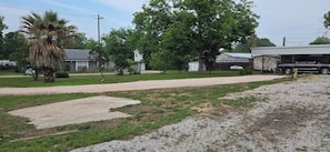 A residential area with a driveway, a palm tree, a large tree, and a house with a garage. - Hidden Cove RV Site On Lake LBJ. (Kingsland)