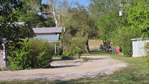 A gravel driveway leading to a house with a metal roof, surrounded by trees and greenery. - Hidden Cove RV Site On Lake LBJ. (Kingsland)