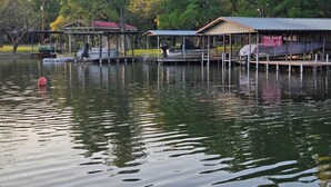 A calm lake with docked boats, a red buoy, and a 'For Sale' sign on a building. - Hidden Cove RV Site On Lake LBJ. (Kingsland)