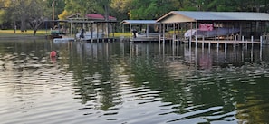 A calm lake with docked boats, a red buoy, and a 'For Sale' sign on a building. - Hidden Cove RV Site On Lake LBJ. (Kingsland)