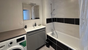 Une salle de bain moderne équipée d’un lave-linge, d’un évier et d’une douche.