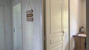 Un couloir avec des portes blanches, un panneau fixé au mur et une petite table en bois décorée d’un motif représentant un pingouin.