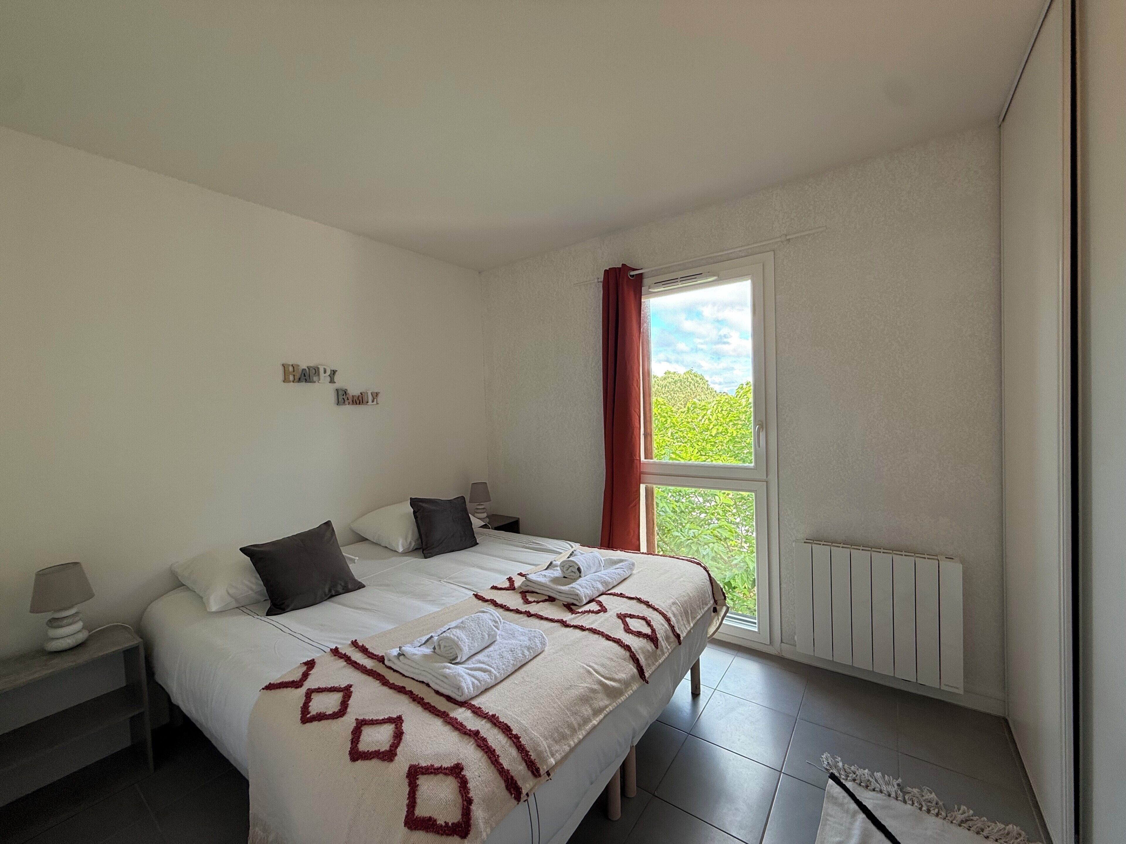 Een slaapkamer met een bed, twee nachtkastjes, een raam met uitzicht en een muur met een 'Happy Family' bord.