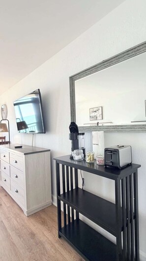 A modern room with a flat-screen TV, a coffee maker, a toaster, and a mirror on the wall. - Sunrise & Waves Ocean Front Studio, Pool (Myrtle Beach)