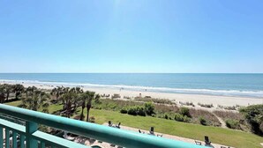 Blick auf einen Strand von einem Balkon mit Pool, Palmen und blauem Himmel.
