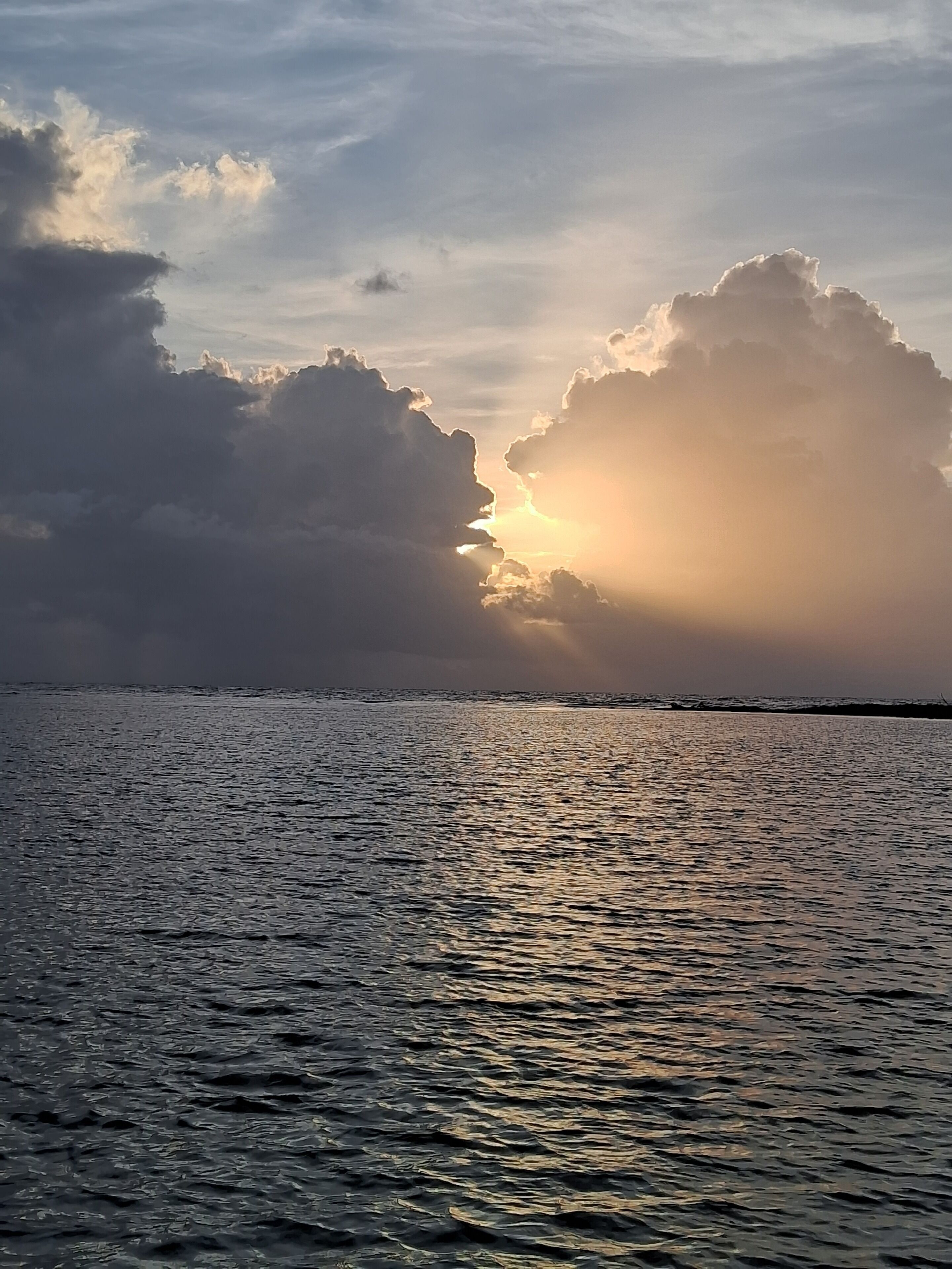 A body of water reflecting sunlight with large clouds in the sky.