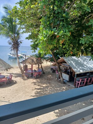 A beachside area with a thatched-roof hut, a small bar, and a seating area with tables and chairs.