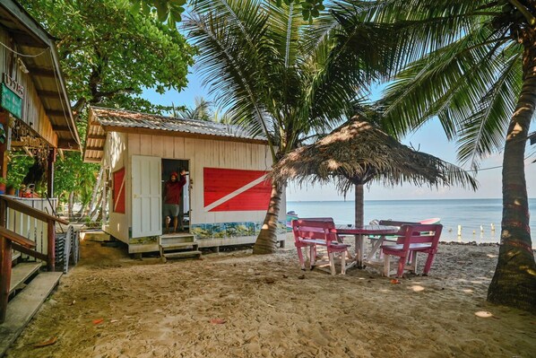 A beachside shack with a thatched roof, a small table with chairs, and a view of the ocean. - Blue Horizon Studios  (Roatan)