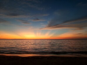 A sunset over a calm sea with a beach in the foreground. - Blue Horizon Studios  (Roatan)