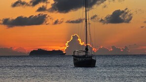 A sailboat on calm waters with a sunset and a ship in the background.