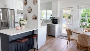 A modern kitchen with white cabinets, a stainless steel refrigerator, a built-in microwave, and a dining area with wicker chairs and a table. - 3 bedroom & 2 bathroom home in Glendora, CA with a pool and spa/hot tub (Glendora)