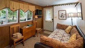 A room with a bed, a desk, a chair, a television, and a door.