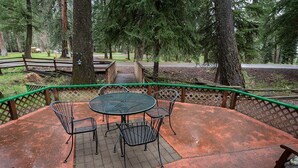 A covered outdoor patio with a round table and chairs, surrounded by a green fence.