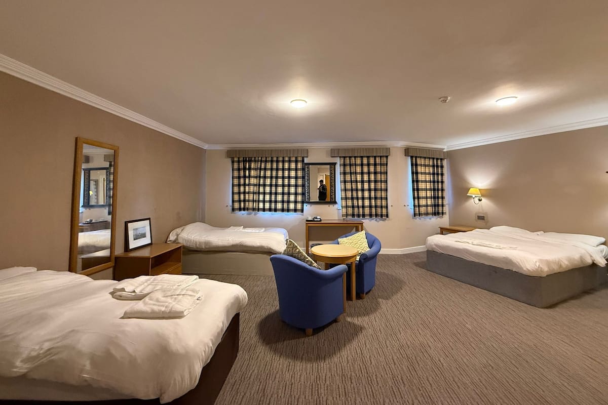 Una habitación de hotel con dos camas, un escritorio, una silla, un espejo y una ventana con cortinas.