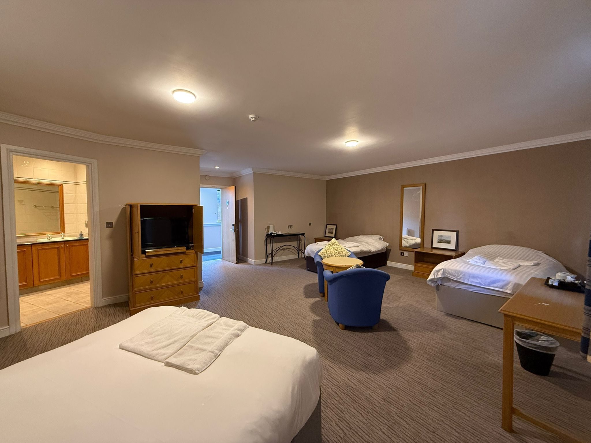 A hotel room with a large bed, a television, a desk, a chair, and a bathroom visible through an open door.