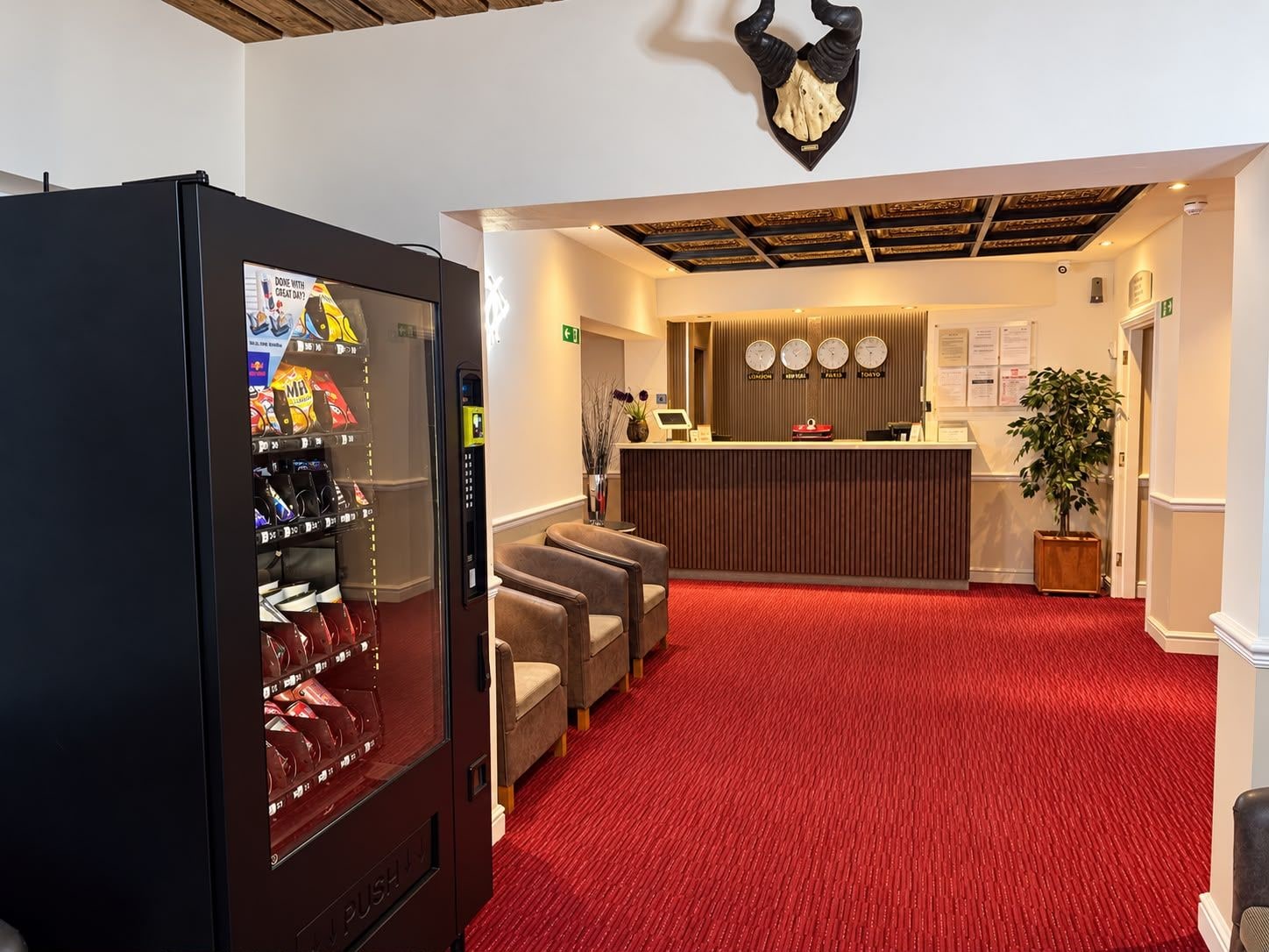 A hotel reception area with a red carpet, a reception desk, and a vending machine.
