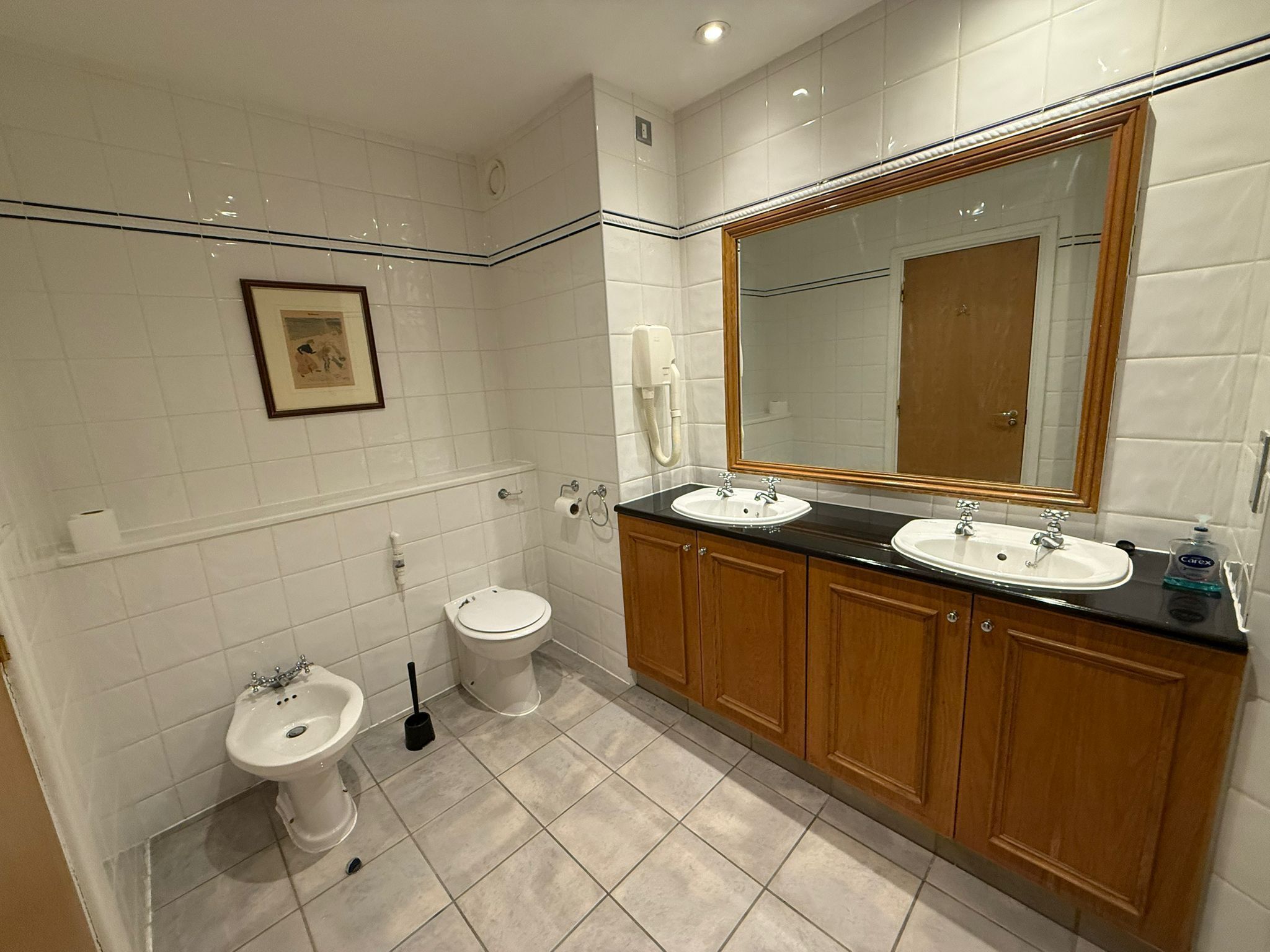 Une salle de bain avec deux lavabos, des toilettes, un bidet et un grand miroir.