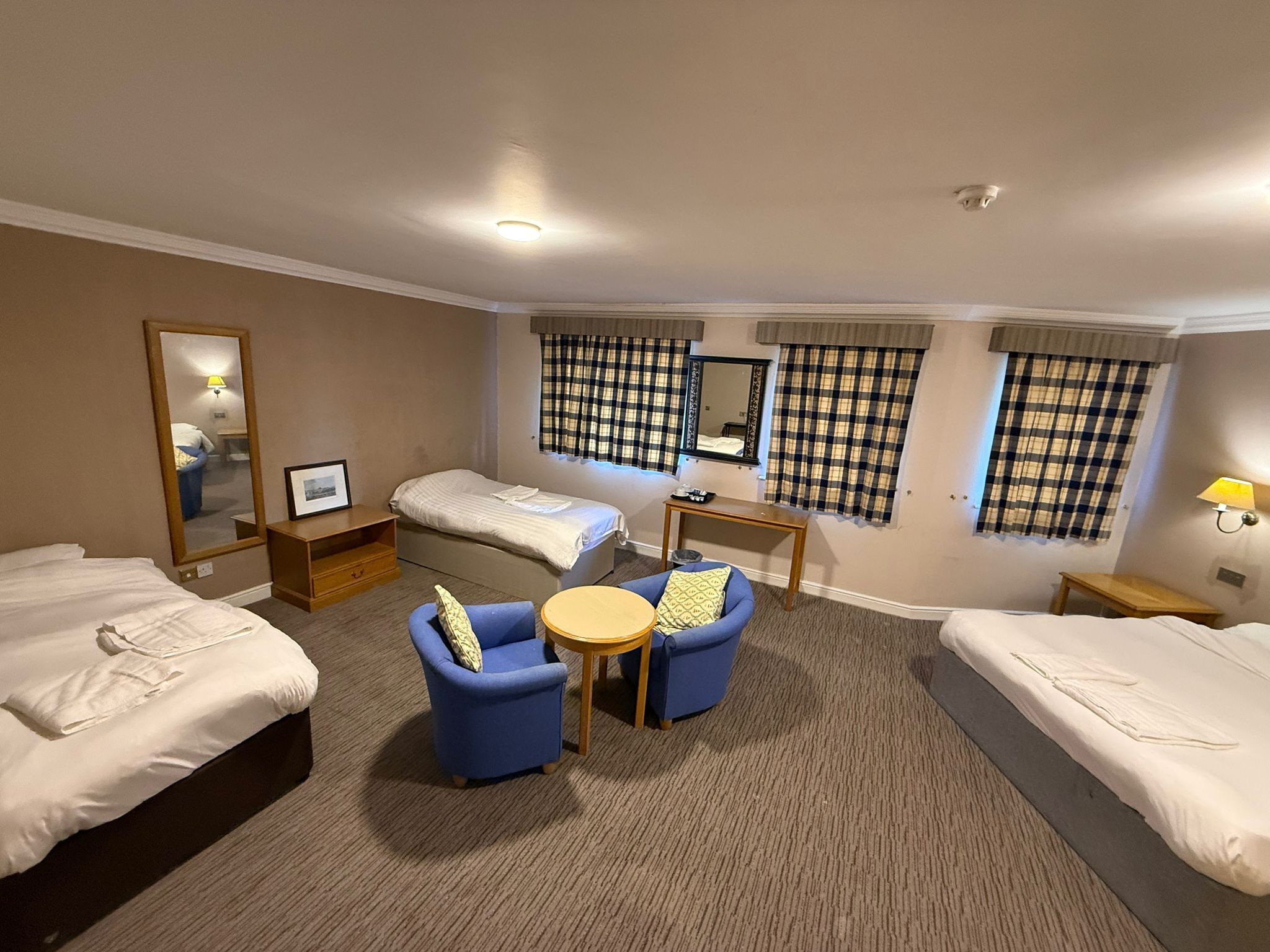 A hotel room with two single beds, a sofa, a small table, a mirror, and plaid curtains.