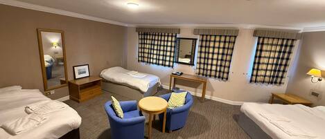 A hotel room with two single beds, a sofa, a small table, a mirror, and plaid curtains.