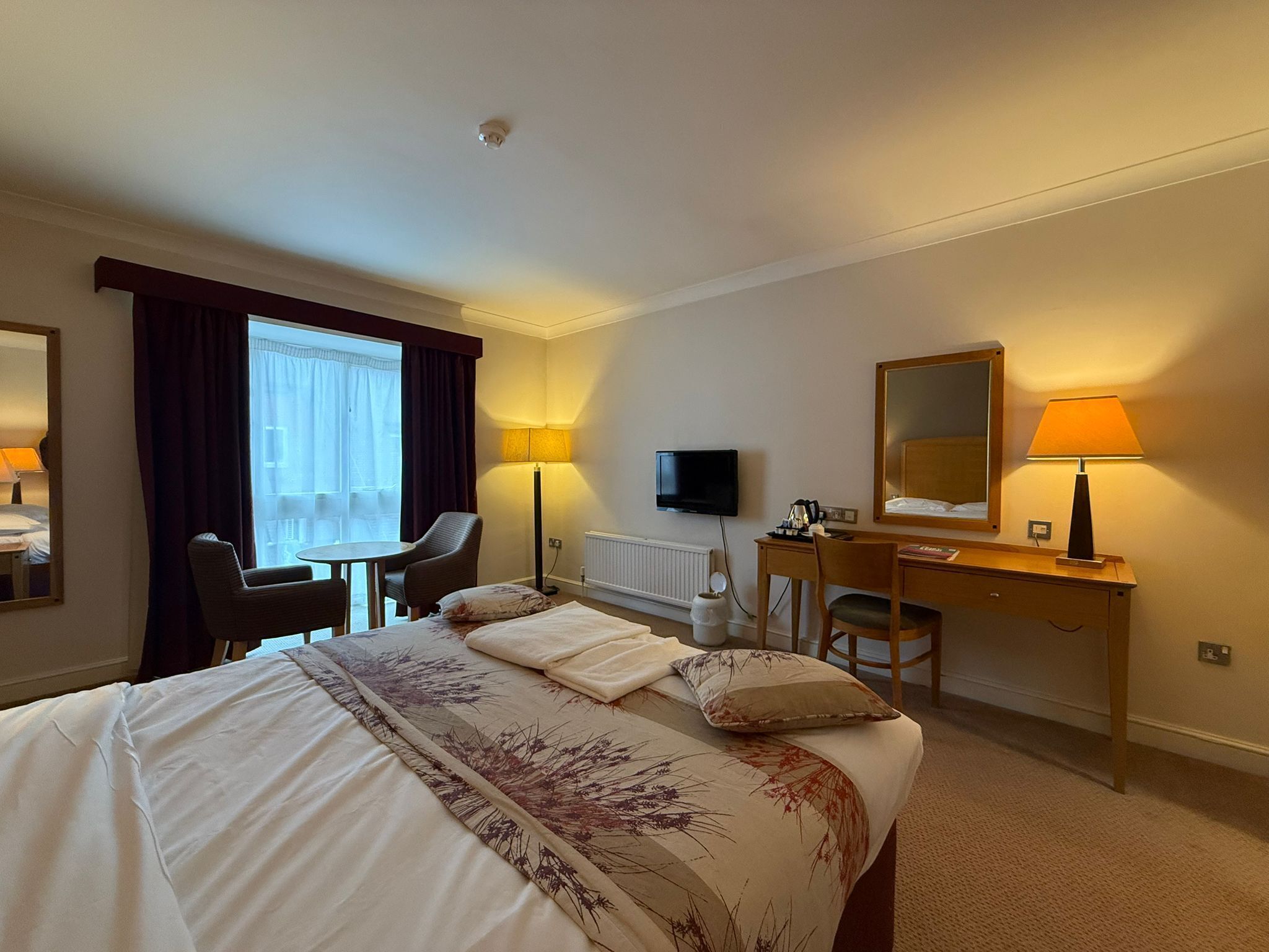 Une chambre d’hôtel équipée d’un lit, d’un bureau, d’une chaise, d’une télévision et d’une fenêtre avec des rideaux.