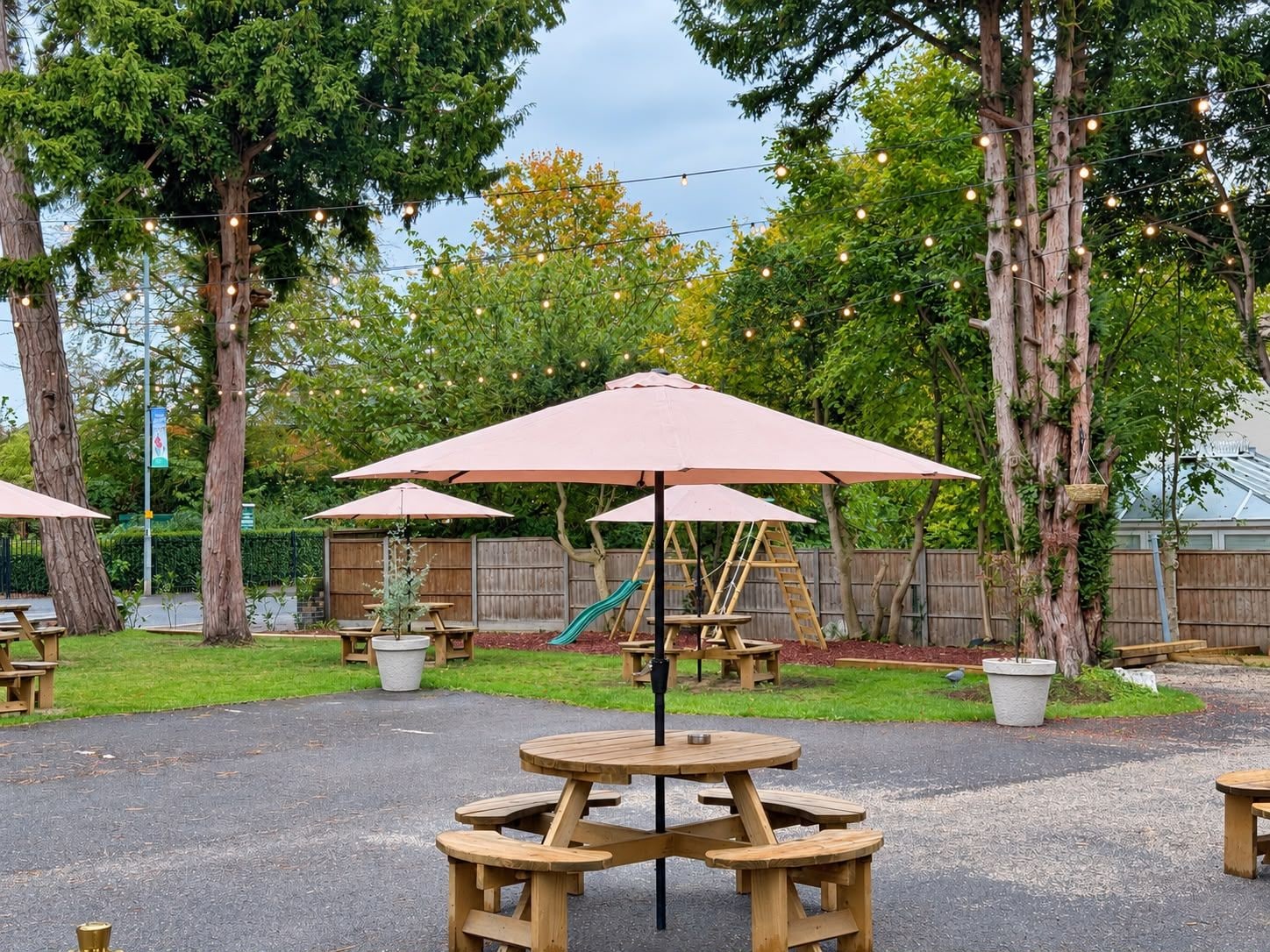 Un espacio al aire libre con mesas de picnic y sombrillas, rodeado de árboles y una valla de madera.