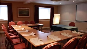 A conference room with a long table, red chairs, a projector screen, and a painting on the wall.