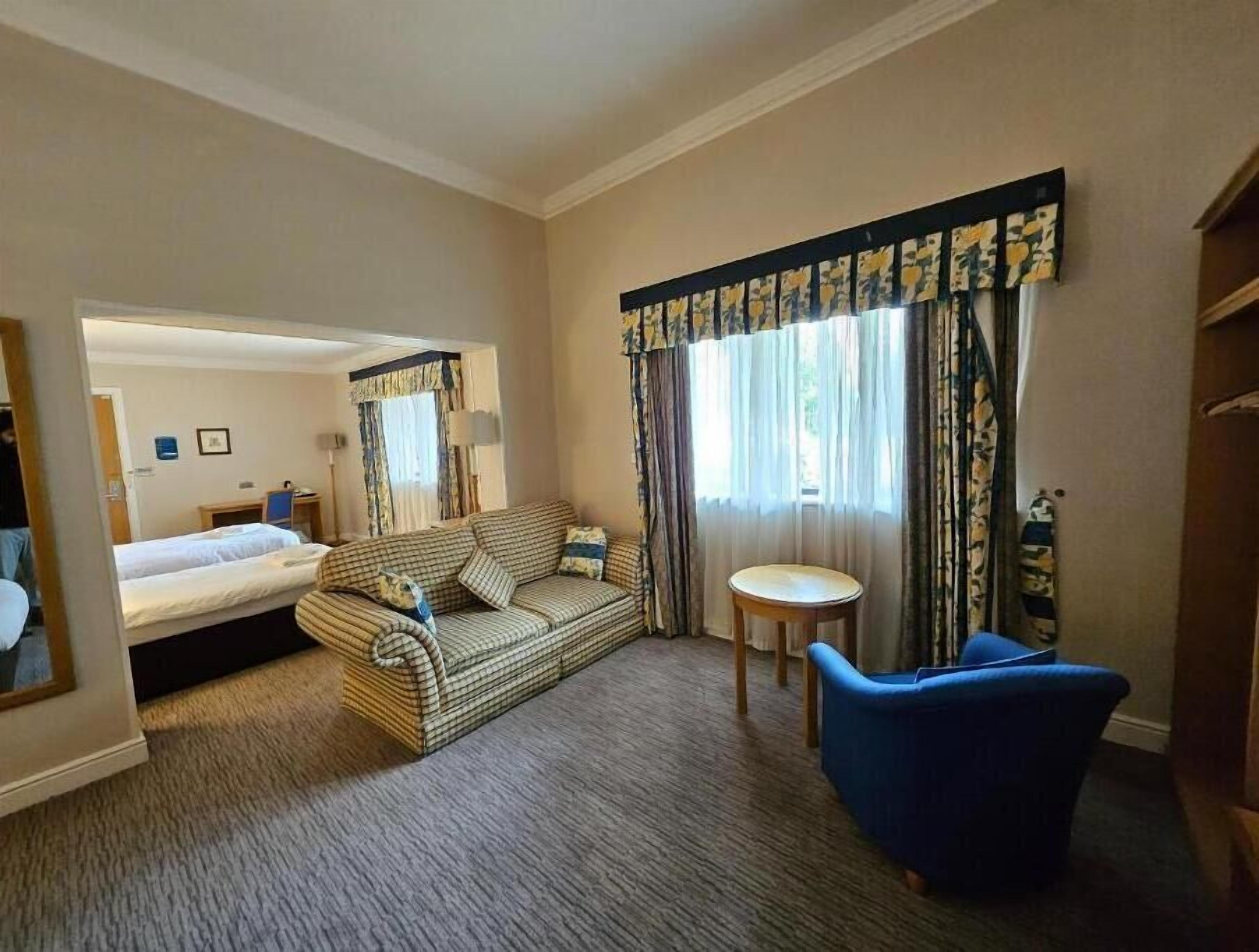 A hotel room with a bed, a sofa, a chair, a small table, and a mirror.