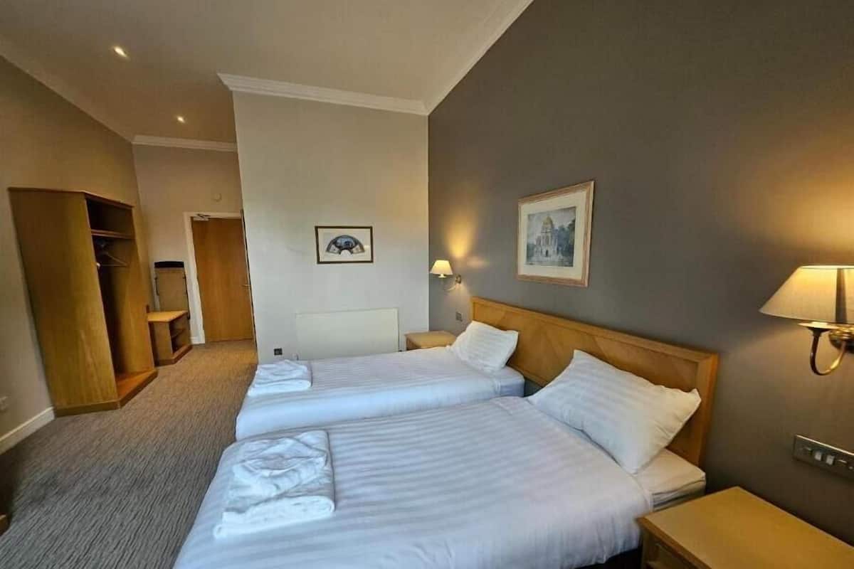Habitación de hotel con dos camas, un armario de madera, un escritorio y una lámpara fijada a la pared.